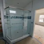 Modern glass shower enclosure with blue accent tiles in a bathroom under construction.