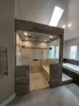 Modern glass-enclosed shower with wood accents and recessed lighting.