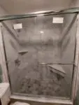 Modern glass shower enclosure with gray tile walls and corner shelves.