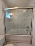 Glass shower door with a sliding mechanism in a bathroom.